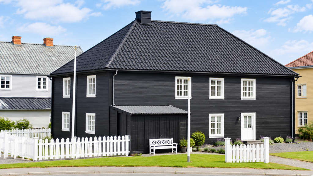 Dark exterior house with white-trimmed windows, tiled roof, and white picket fence